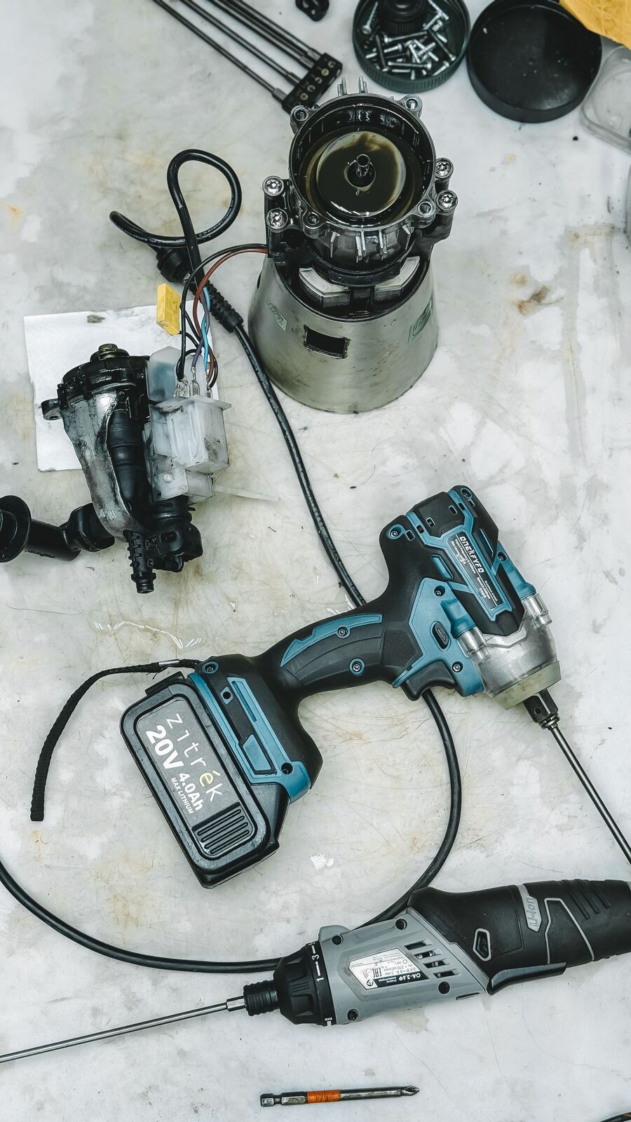 Cordless drivers beside a disassembled blender motor and appliance pump on a workbench